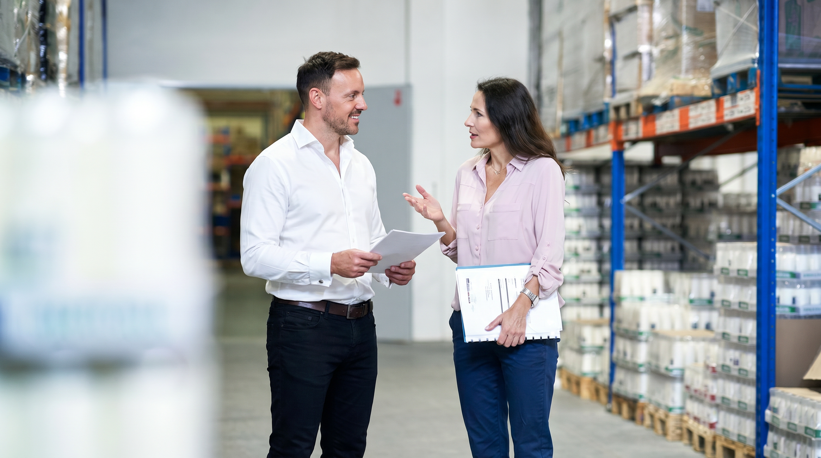 Two colleagues reviewing paperwork on a warehouse floor.